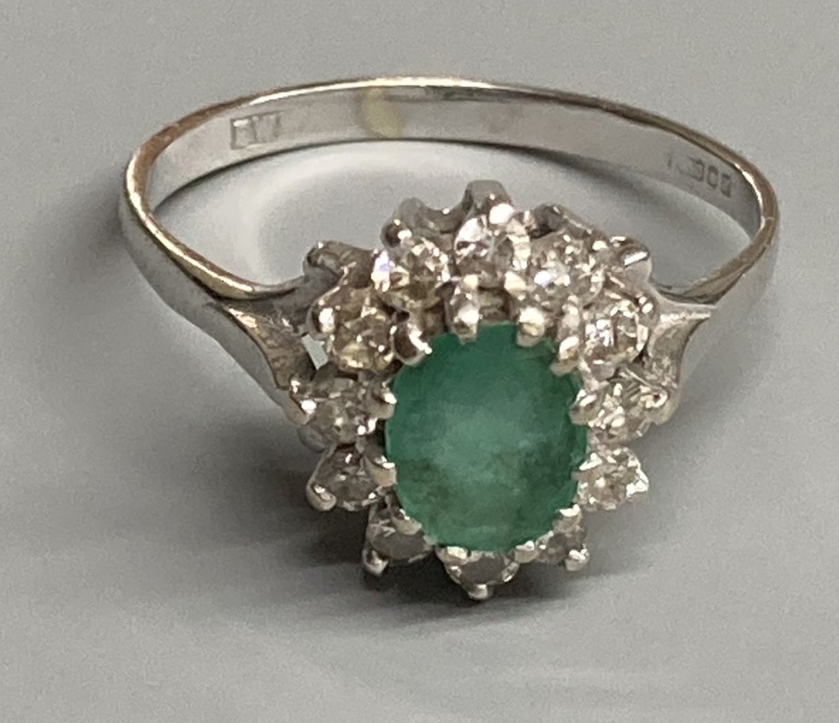 A modern 18ct white gold, emerald and diamond set oval cluster ring, size O/P, gross 3.6 grams.