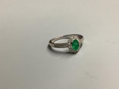 A modern 18ct white gold, emerald and diamond set oval cluster ring, with diamond set shoulders,