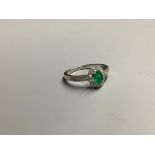 A modern 18ct white gold, emerald and diamond set oval cluster ring, with diamond set shoulders,