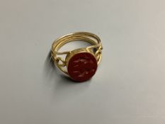 A yellow metal and carved oval Jasper set signet ring, with pierced shank, the matrix carved with