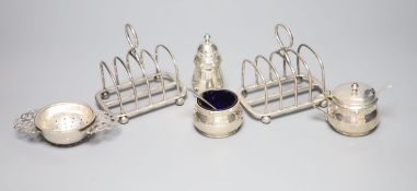 A pair of George V silver toast racks, a silver tea strainer and a silver three piece condiment