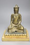 A South East Asian engraved and polished bronze figure of a seated deity,on stepped giltwood