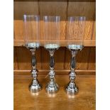 Set of three nickel plated candle stands with glass shades, height 51cm