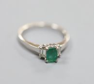 A modern white metal (engraved 750), emerald and diamond set three stone ring, size P,gross weight