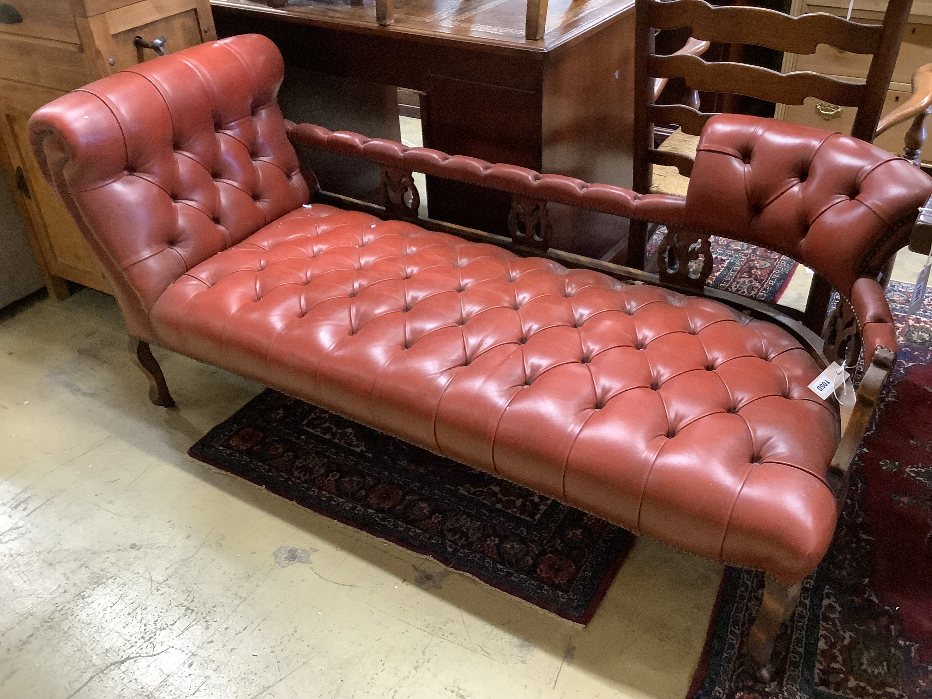 An Edwardian beech two-seater couch upholstered in buttoned burgundy hide on scrolled legs, length