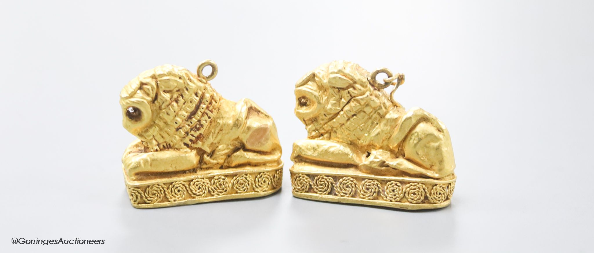 A pair of Etruscan style yellow metal recumbent lion pendant charms, 25mm, gross 11.1 grams.