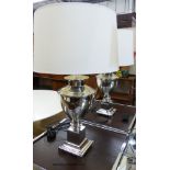 A pair of chrome urn form table lamps with cream shades by Andrew Martin,on square plinths and