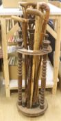 A circular turned beech stick stand, containing various walking sticks and a shooting stick