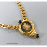 A modern curb link yellow metal, inset coin, blue cabochon stone and diamond set pendant necklace,