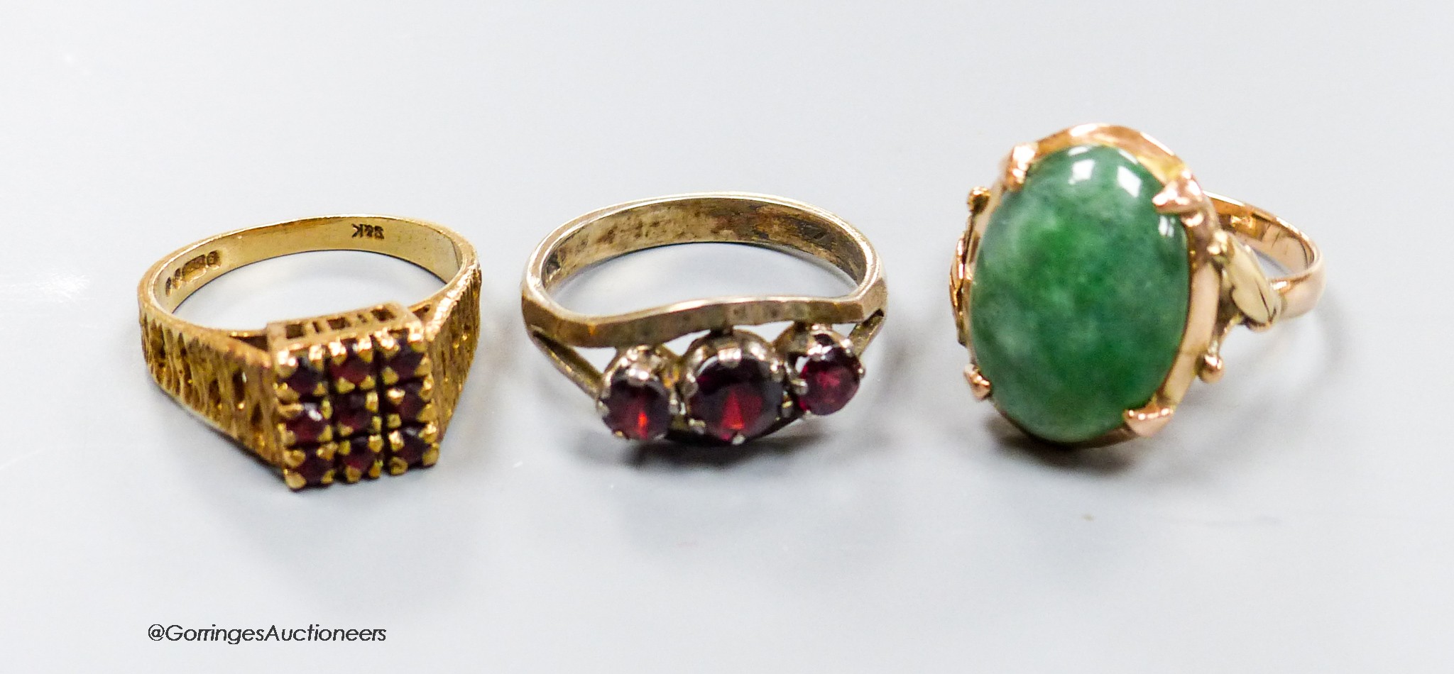 A 9ct gold and garnet cluster ring, a similar white metal ring and a yellow metal and jadeite