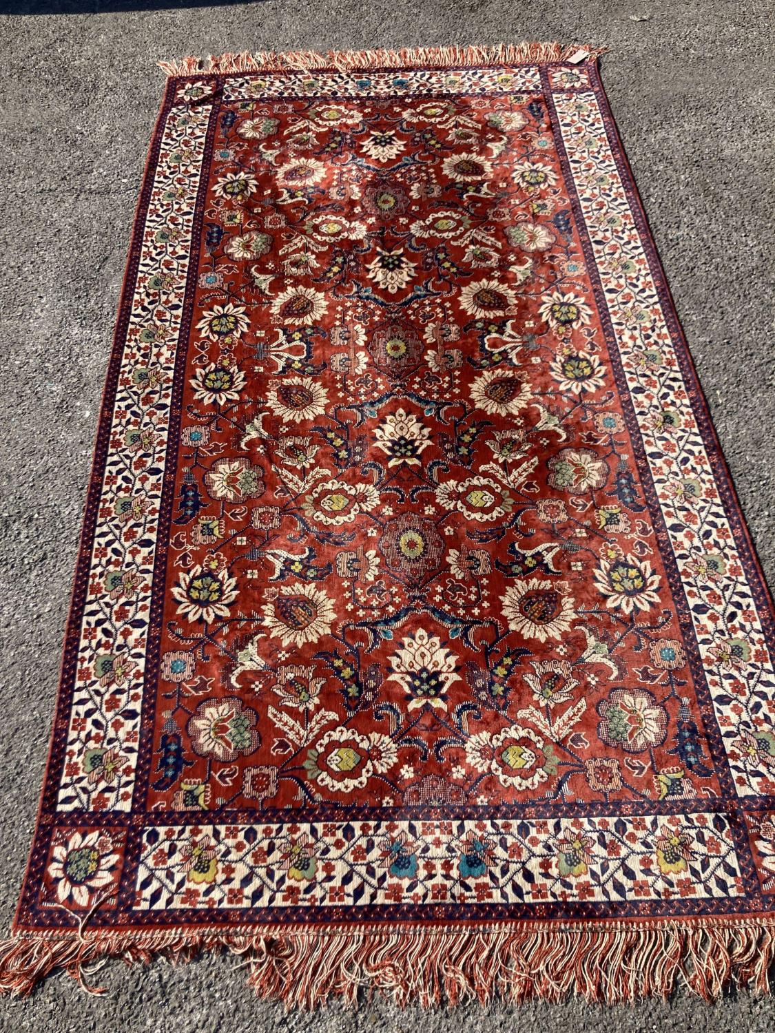 A large embroidered silk rug with a claret red ground interspersed with symmetrical foliate
