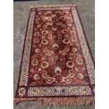 A large embroidered silk rug with a claret red ground interspersed with symmetrical foliate