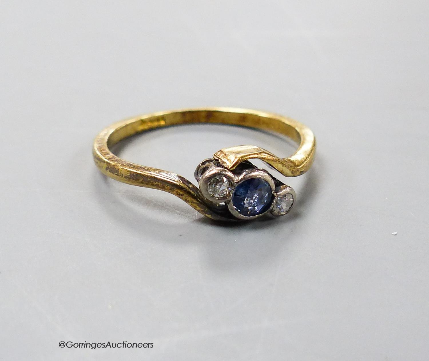 An early 20th century yellow metal, sapphire and diamond set three stone crossover ring, size L,