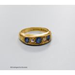 An Edwardian 18ct gold three stone sapphire and two stone diamond set half hoop ring, size M, gross