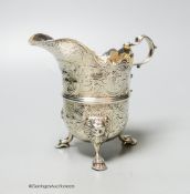 An engraved white metal helmet shaped cream jug, on tripod feet, unmarked, 12.9cm, 9oz.