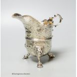 An engraved white metal helmet shaped cream jug, on tripod feet, unmarked, 12.9cm, 9oz.