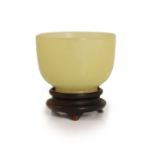 A Chinese yellow hardstone cup, 19th century,5cm diameter, wood stand, rim chip