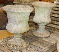 A pair of reconstituted stone campana-shaped urns on stands, decorated with ferns, diameter 34cm,