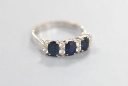 A modern 18ct white gold and three stone sapphire set half hoop ring with diamond set spacers, size