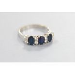 A modern 18ct white gold and three stone sapphire set half hoop ring with diamond set spacers, size