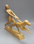 An Art Deco style light elm carving of a woman and dog on lead-weighted plinth, height 40cm