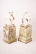 A pair of reconstituted stone horse's heads on plinth bases in the style of Austin and Seeley,