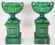 A pair of large dark green glazed terracotta fluted urns, raised on square plinths, diameter 50cm,