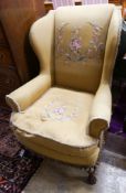 A wing frame armchair, upholstered in gold with embroidered flowers, on carved lion’s paw feet,