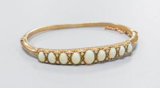 An early 20th century yellow metal and graduated nine stone white opal set hinged bracelet, with