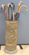 A cylindrical repousse brass stick stand, with walking sticks, parasols, etc.