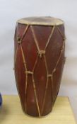 A tall tribal wooden drum, the vellum skins held by bamboo strapping and decorated in red and