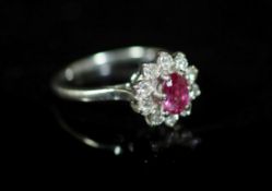 A white gold, ruby and diamond set flower head cluster ring,with central oval cut ruby, size R,