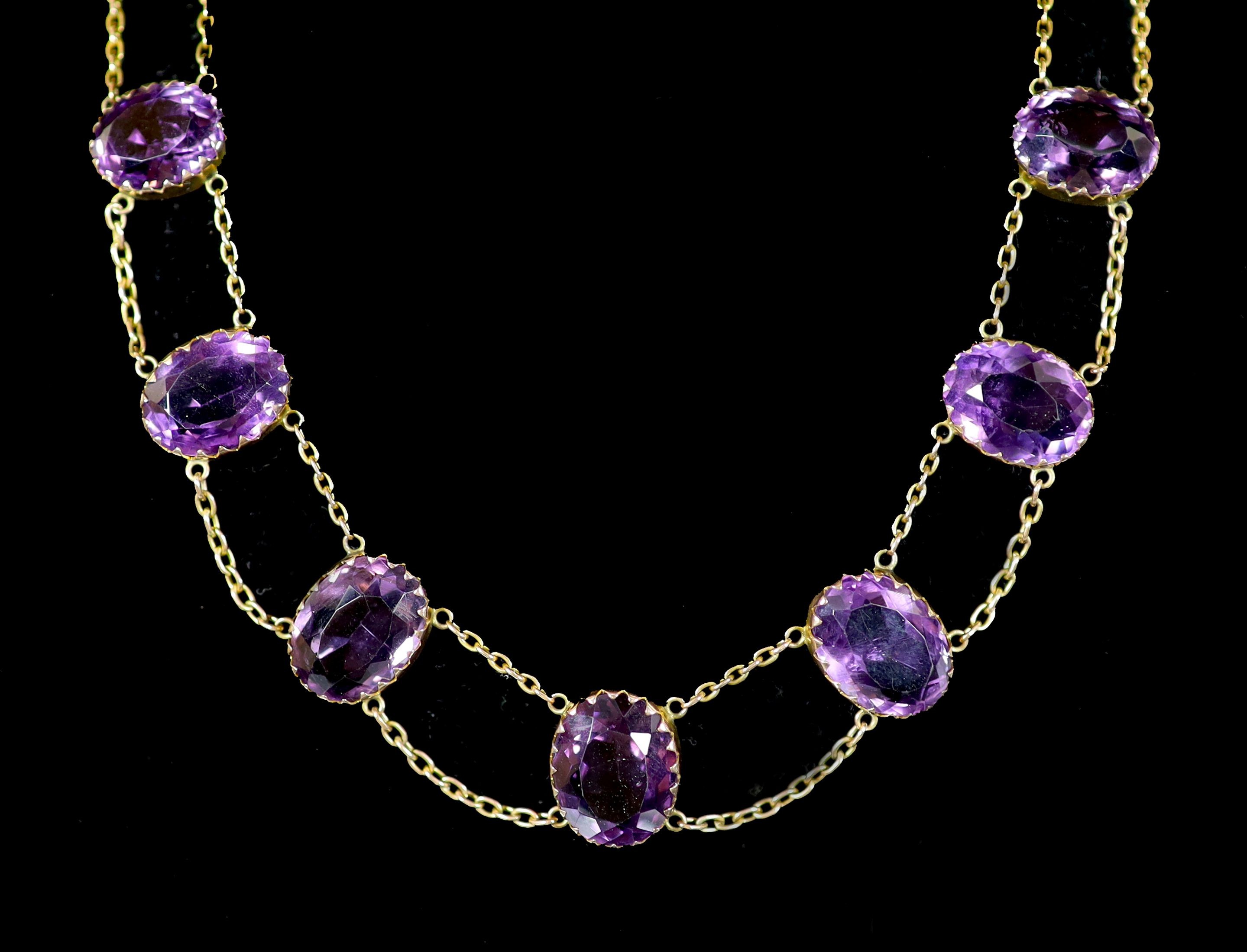 An Edwardian 9ct gold and graduated oval cut amethyst riviere necklace,set with seventeen stones,