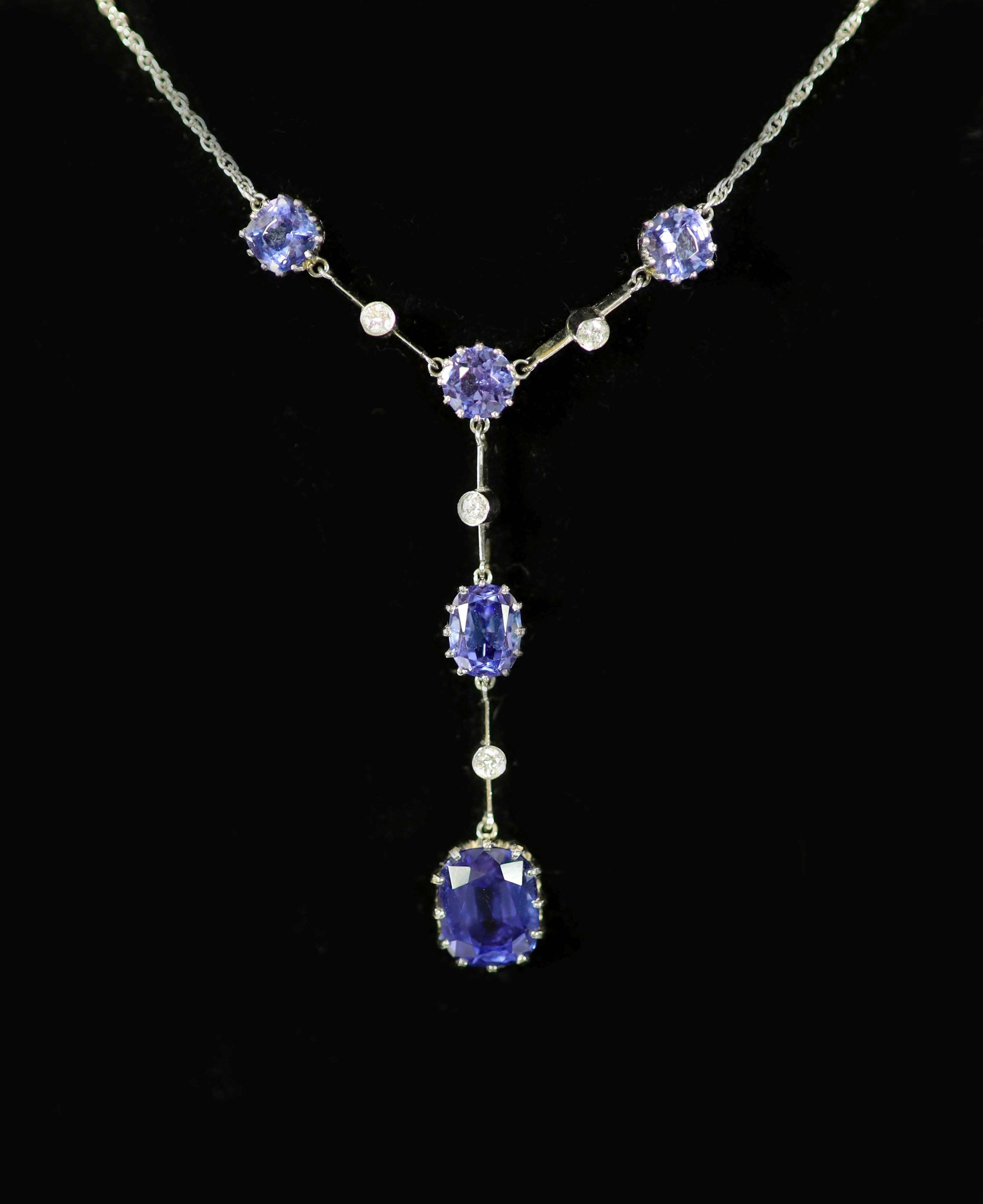 A modern platinum, five stone tanzanite and four small round cut diamond set drop pendant necklace,