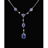A modern platinum, five stone tanzanite and four small round cut diamond set drop pendant necklace,