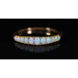 An Edwardian gold and graduated eleven stone white opal set hinged bracelet, with diamond chip