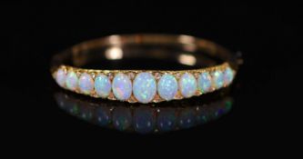 An Edwardian gold and graduated eleven stone white opal set hinged bracelet, with diamond chip