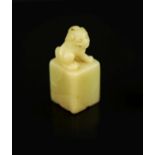 A Chinese inscribed cream coloured soapstone seal,of square section, surmounted by the figure of a