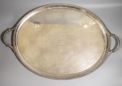 A late Victorian silver oval two handled tea tray, with gadrooned border and engraved inscription,