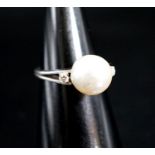 A white metal and single stone cultured pearl dress ring, with diamond set shoulders, size L/M,