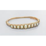An early 20th century gold plated graduated nine stone white opal set hinged bracelet, with