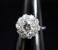 A white metal and eleven stone diamond set flower head cluster ring, the central stone weighing