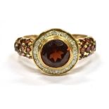 A 9CT GOLD GARNET AND SMALL DIAMOND CLUSTER RING with garnet set shoulders, the central round cut