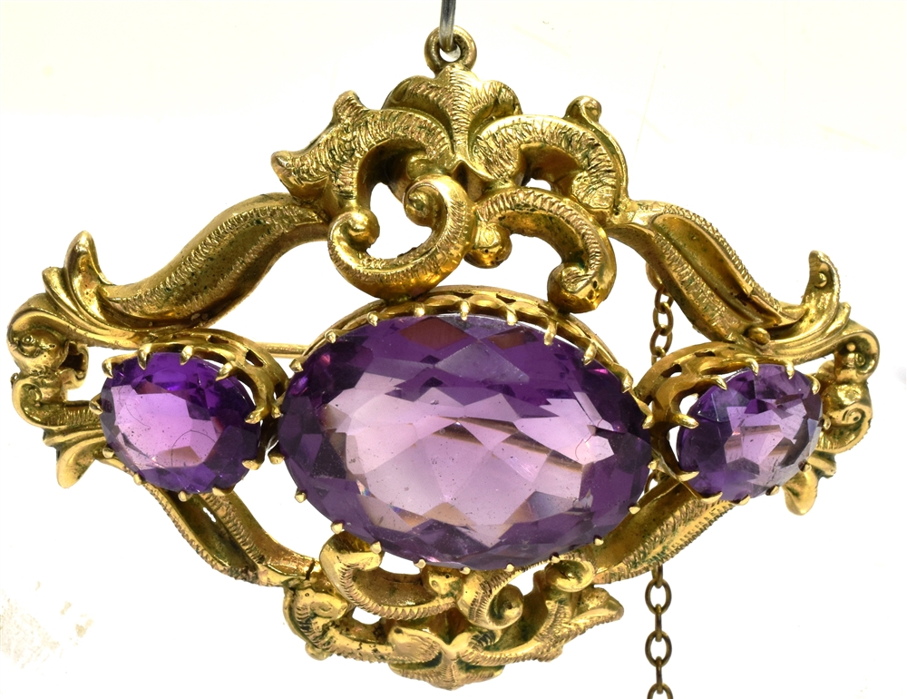 AN AMETHYST THREE STONE SCROLL WORK BROOCH the centre oval amethyst 20mm x 15mm the yellow metal