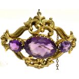 AN AMETHYST THREE STONE SCROLL WORK BROOCH the centre oval amethyst 20mm x 15mm the yellow metal