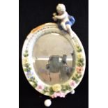 A CONTINENTAL HARD PASTE EASEL BACK OVAL MIRROR with floral decoration and cherub surmount,