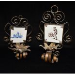 A PAIR OF WROUGHT IRON WALL MOUNTED CANDLESTICKS each housing a Dutch Delft tile, the tiles 13cm