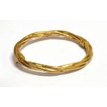 A 9CT GOLD HINGED BANGLE the barley twist design of hollow construction with sprung clasp,
