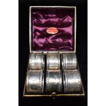 A CASED SET OF 6 SILVER NAPKIN RINGS Of plain form with applied waved boarder, crests to each and