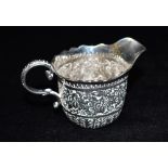 A VICTORIAN SMALL SILVER CREAM JUG Of helmet form all over embossed floral and scroll decoration,